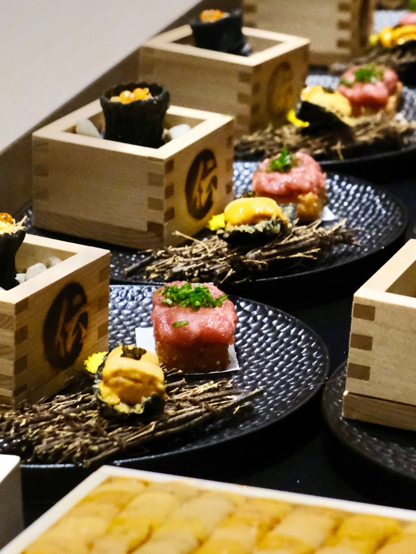 Wooden masu cups and tartare bites on black plates, seen from the side