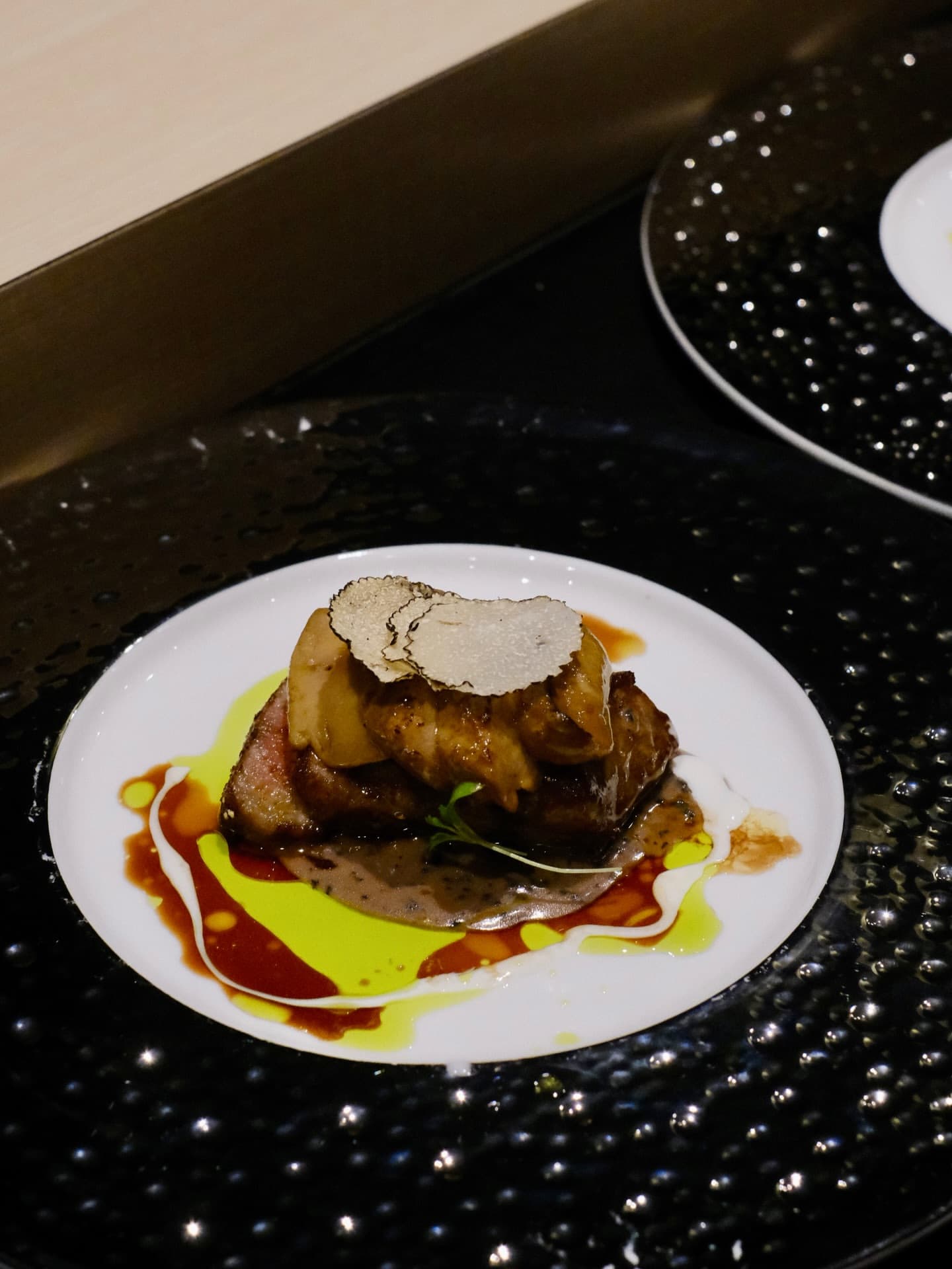 A braised course with shaved truffle and two sauces on a white plate