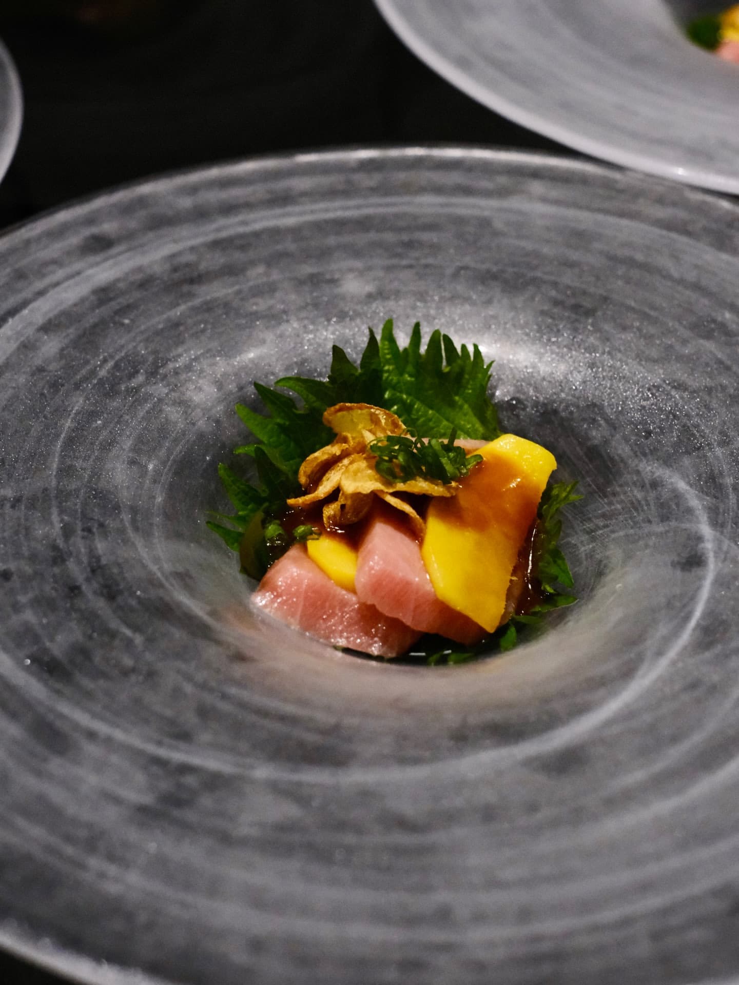 Slices of tuna with mango and shiso leaf on a swirl-glazed plate